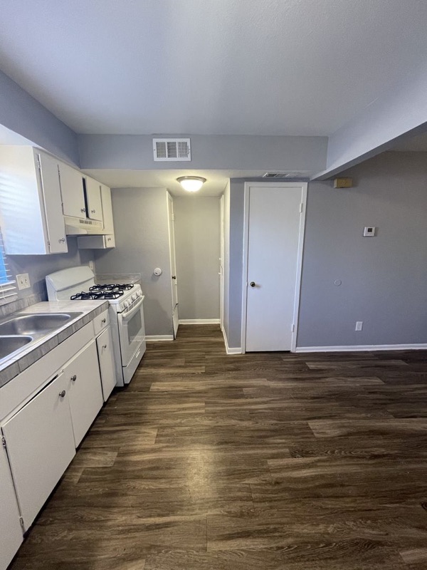 A La Bella kitchen with white cabinets, a gas range and plank flooring running through to the hallway.
